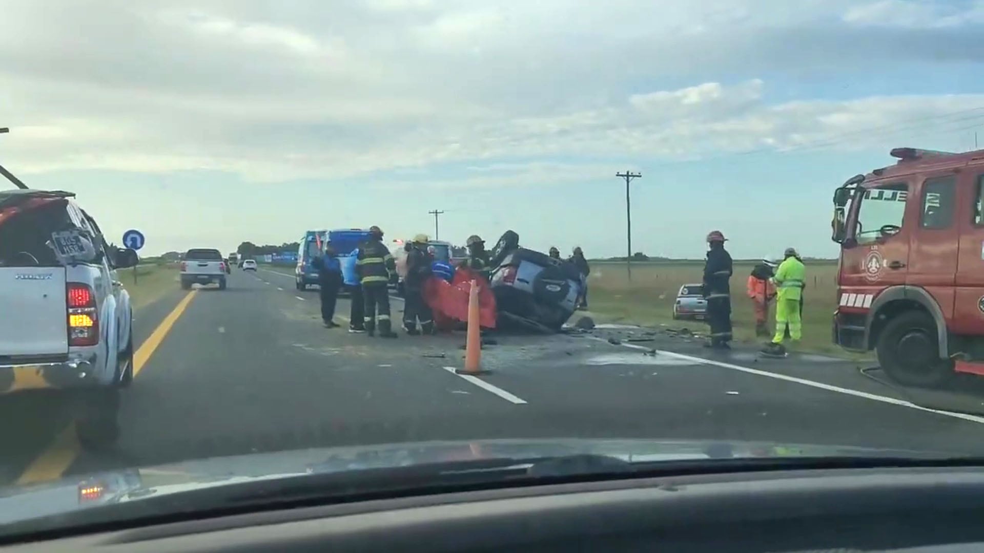 Personal de emergencia atiende un accidente vehicular en la Ruta 2, donde un coche ha volcado y se observa la presencia de un camión de bomberos y rescatistas. (Captura de video)