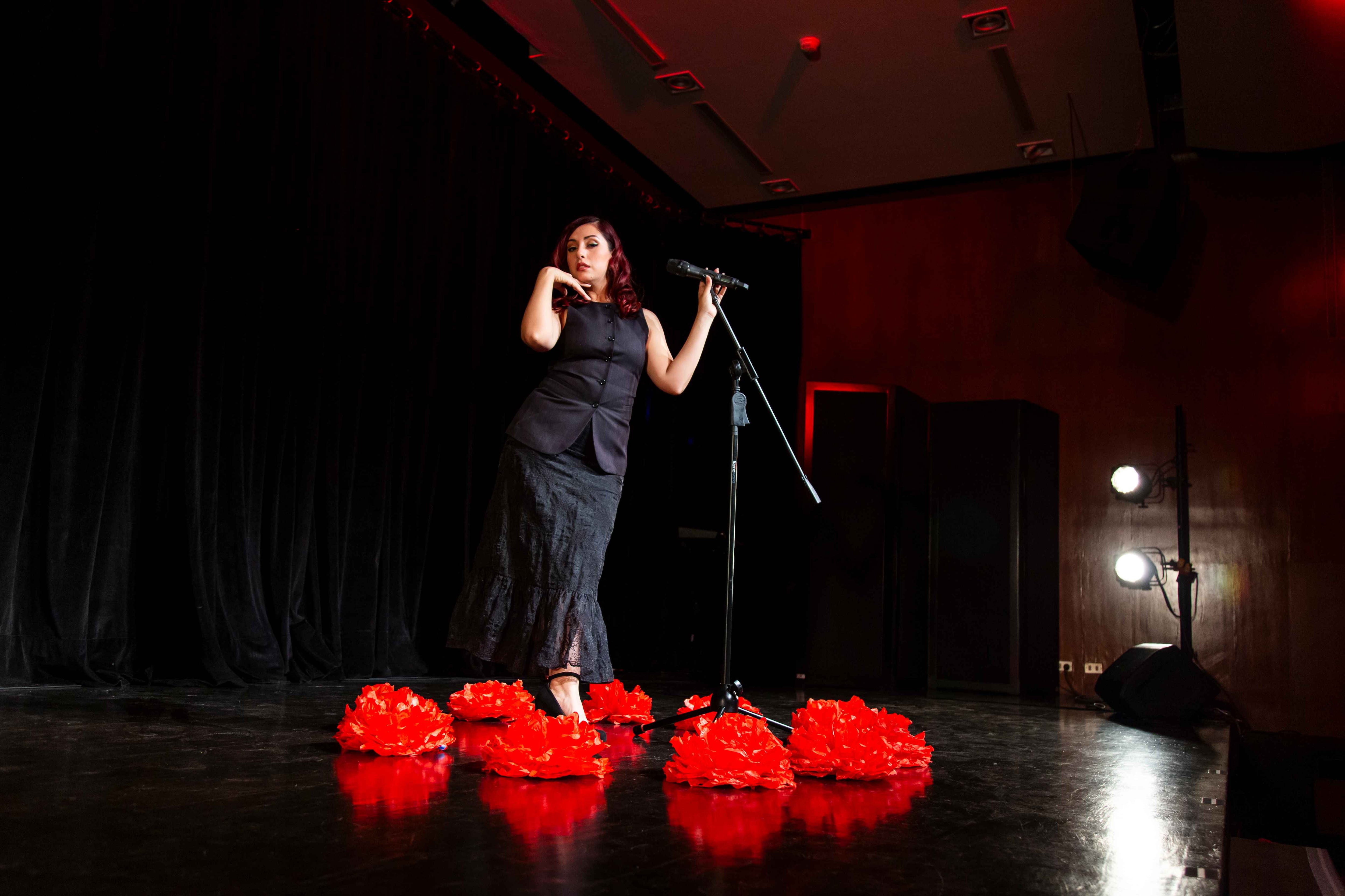 La cantante Priss Arévalo interpreta un homenaje a Mon Laferte sobre un escenario decorado con flores rojas en el Británico Cultural.