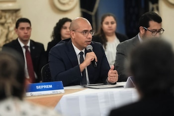 Un hombre con anteojos y traje habla por un micrófono sentado a una mesa con un letrero azul que dice SEPREM
