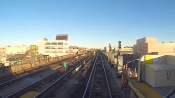 Vista elevada de múltiples vías de tren que se extienden en un entorno urbano con edificios de varios pisos bajo un cielo azul claro