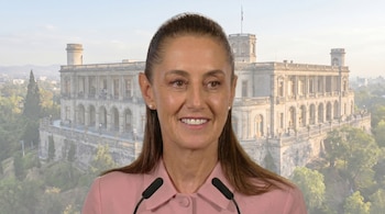 Claudia Sheinbaum, con camisa rosa y cabello recogido, sonríe ante dos micrófonos, con el Castillo de Chapultepec, incluyendo una bandera mexicana, difuminado detrás.