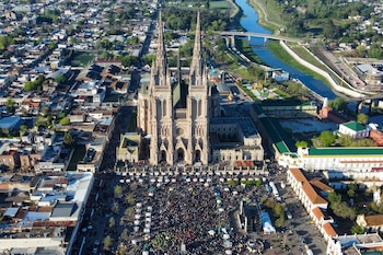 Vista aérea de una basílica gótica con una multitud congregada en la plaza exterior y un río al costado