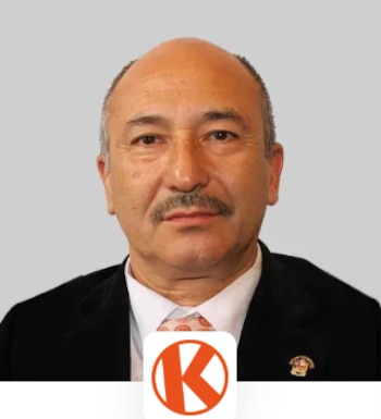 Retrato de un hombre de saco negro, camisa blanca y bigote, con un logotipo naranja de una letra K dentro de un círculo en la parte inferior