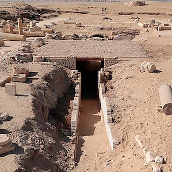 Entrada a una tumba en el sitio arqueológico de Oxirrinco, en un paisaje desértico con ruinas antiguas dispersas y columnas de piedra