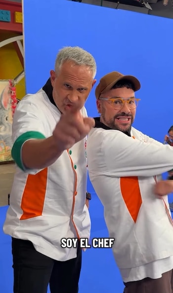 Dos hombres, Arath de la Torre y Shiky, posan en chaquetas de chef blancas con detalles naranjas sobre un fondo azul. Arath apunta al frente