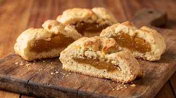 Cuatro panes dulces rellenos con dulce de batata, uno cortado por la mitad, sobre una tabla de cortar de madera con migas y fondo de madera.