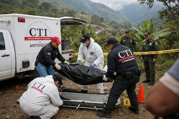 Cinco hombres, tres del CTI y dos policías, manejan un cuerpo en bolsa negra, camilla, vehículo forense CTI, cinta "Escena del Crimen", cono naranja.