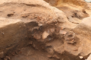 Fosa de excavación en terreno arenoso con restos de piezas cerámicas rotas incrustadas entre diferentes estratos de tierra