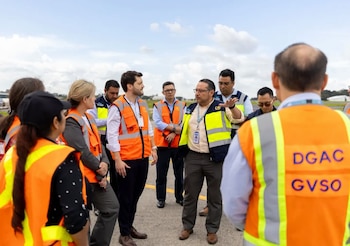 Grupo de doce personas en exteriores, la mayoría con chalecos de seguridad naranjas y amarillos, de pie sobre una superficie de cemento bajo un cielo nublado