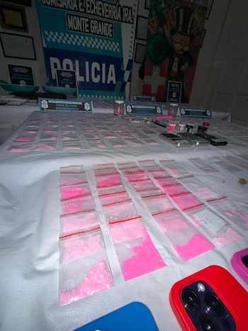 Mesa blanca cubierta con decenas de bolsas pequeñas de cierre hermético llenas de polvo rosa (tusi), junto a balanzas, teléfonos móviles y documentos policiales