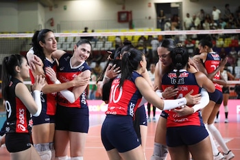 Varias jugadoras de voleibol de la Universidad San Martín, vestidas de rojo y azul, se abrazan sonrientes en el centro de la cancha celebrando su victoria