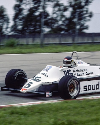 Un coche de Fórmula 1 blanco con el número 5, pilotado por Carlos Reutemann, acelera en una pista de carreras, con árboles borrosos y hierba verde de fondo