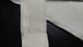 Primer plano de un delgado alambre oscuro sobre una gasa blanca, con un fondo negro texturizado