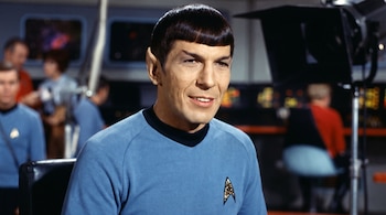 Leonard Nimoy con orejas puntiagudas y uniforme azul de Star Trek en un plató de televisión con pantallas y focos al fondo.