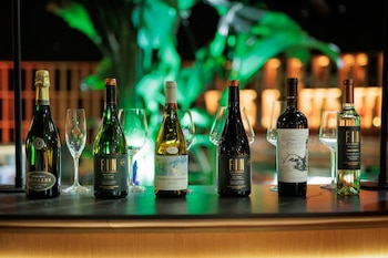 Seis botellas de vino alineadas sobre una barra oscura, acompañadas por cinco copas de cristal vacías al fondo