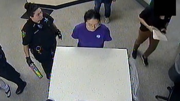 Vista aérea: oficial con detector de metales inspecciona a persona en camiseta morada detrás de mostrador blanco en un interior