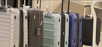 Hilera de maletas de colores gris, negro, celeste y azul sobre una cinta transportadora con sus asas extendidas