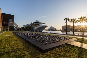 Una plataforma con esferas en el césped junto a un crucero, la Ópera de Sídney, palmeras y el Museo de Arte Contemporáneo