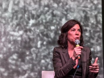 María O'Donnell, con cabello oscuro y chaqueta marrón, habla en un micrófono Shure durante una presentación frente a un fondo texturizado gris