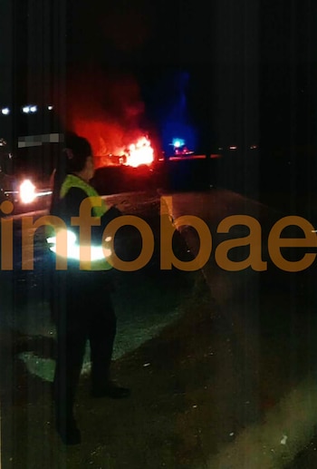 Una persona con chaleco reflectante observa un incendio en la oscuridad de la noche, con grandes llamas y luces de emergencia rojas y azules