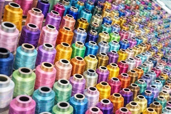 Cientos de bobinas de hilo de coser en colores vibrantes, como azul, verde, amarillo, naranja, rosa y morado, organizadas en filas diagonales y muy juntas.