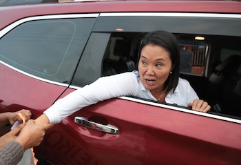 Keiko Fujimori, con camisa blanca, se asoma por la ventana de un vehículo rojo y estrecha la mano de una persona. Tiene la boca abierta