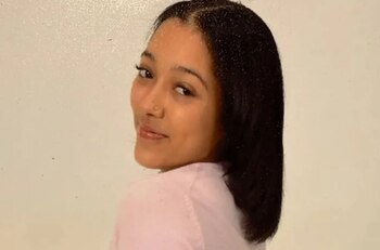 Primer plano de una mujer joven de cabello oscuro y camiseta rosa claro, mirando por encima del hombro hacia la derecha con un fondo blanco liso