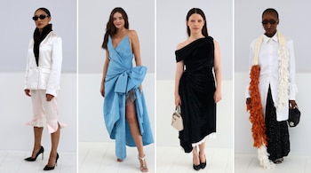 Cuatro mujeres posan con un traje blanco, un vestido azul con lazo, un vestido negro y un atuendo blanco con bufanda larga.