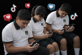 Tres estudiantes de secundaria con uniforme escolar (dos chicos, una chica) miran sus smartphones contra un fondo negro, con iconos 3D de TikTok y corazones.