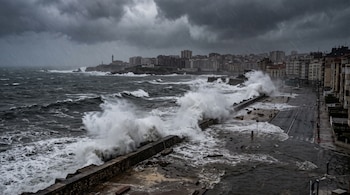 Olas rompen contra un malecón e inundan una calle urbana bajo un cielo gris con lluvia