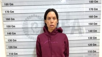 Una mujer con sudadera bordó posa frente a un fondo con escala de estatura graduada en centímetros de 110 a 180