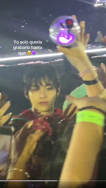 Taehyung se acerca al público en un concierto mientras varios asistentes extienden las manos y sostienen una linterna luminosa