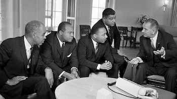 Fotografía en blanco y negro de cinco hombres con traje en un salón. El presidente de EE. UU. Lyndon B. Johnson gesticula mientras otros líderes escuchan