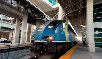 Un tren de pasajeros azul y verde con el número 822 en el frente está estacionado en una plataforma de estación con una franja amarilla y pilares de concreto