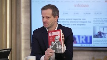 Un hombre con traje oscuro y camisa blanca, usando un micrófono de diadema, gesticula mientras habla. De fondo, una pantalla con el logo de Infobae