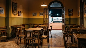 Interior con mesas y sillas de madera, lámpara encendida y puerta abierta hacia una cancha de bochas desierta con marcador en cero.