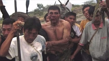 Un hombre semidesnudo y con sangre en el rostro es sostenido por varios hombres nativos, algunos con lanzas, en un entorno natural