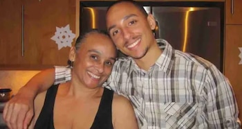 Una mujer con camiseta negra y un hombre con camisa a cuadros sonríen juntos en una cocina frente a un mueble de madera