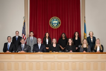 Once personas en una sala de audiencias con estrado de madera, telón rojo, banderas de Estados Unidos y Delaware, y el sello de la Corte de la Cancillería visible