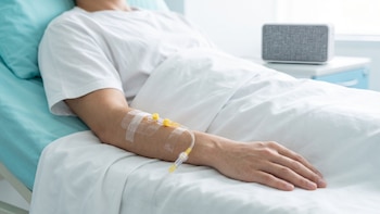 Un hombre acostado en una cama de hospital con un catéter intravenoso sujeto con cinta adhesiva en el brazo derecho