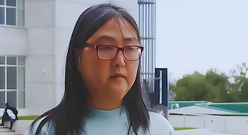 Una mujer con anteojos de marco rojo y cabello largo viste una camisa celeste frente a un edificio blanco