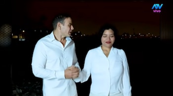 Un hombre y una mujer, Mark Vito y Leslie Echevarría, caminan lado a lado por la noche. Ambos visten camisas blancas de manga larga