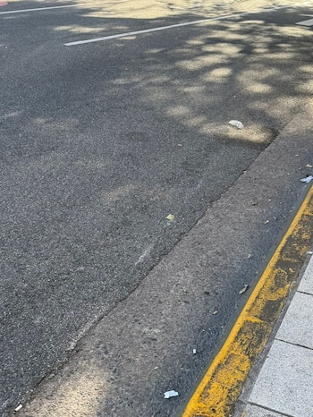 Primer plano de una sección de asfalto gris oscuro con un bordillo de hormigón desgastado pintado de amarillo, y una franja de acera