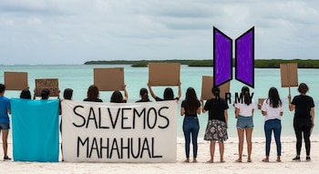 Jóvenes de espaldas en playa blanca sostienen pancartas y manta 'Salvemos Mahahual', frente a mar turquesa y manglares. Se ve un logo violeta de ARMY de BTS.