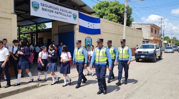 Policiais de casaca amarela caminham pela calçada com estudantes uniformizados saindo de uma escola em Tegucigalpa, Honduras.