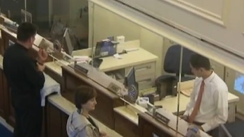 Tres personas en una oficina: un hombre de negro de espaldas, una mujer de chaqueta clara de perfil y un hombre de camisa blanca con corbata roja ante un monitor