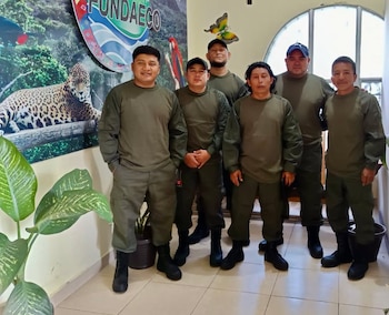 Seis hombres con uniforme verde oliva y botas negras de pie junto a un panel con la palabra FUNDAECO y la figura de un jaguar