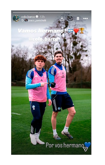 Colo Barco y otro futbolista, ambos con petos de entrenamiento rosas y equipación azul, posan en un campo de fútbol con árboles de fondo. Barco señala hacia el otro jugador