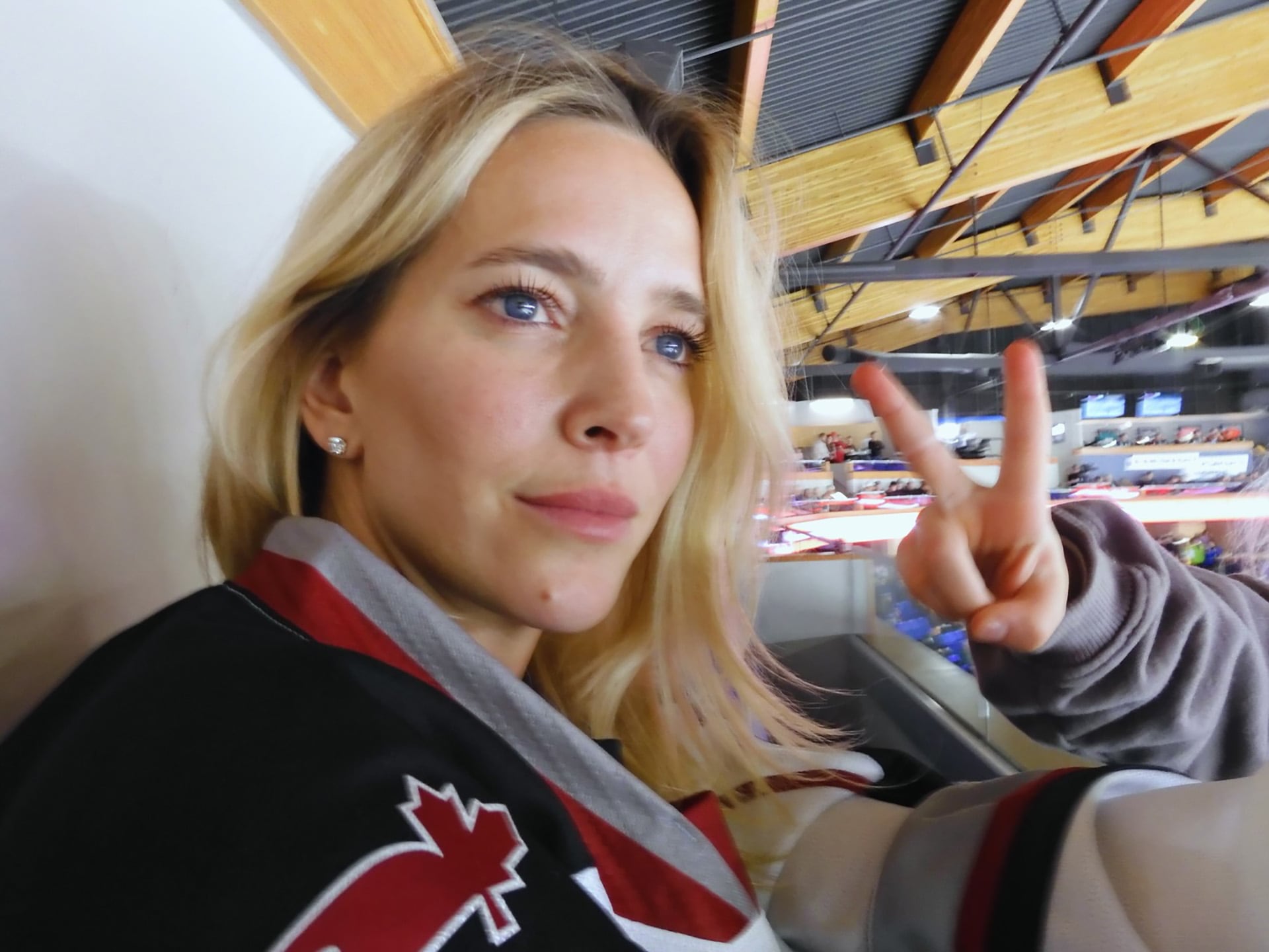 La actriz Luisana Lopilato expresa su entusiasmo por el hockey sobre hielo haciendo un gesto de victoria desde las gradas de un estadio.