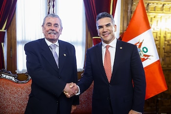 Dos hombres en traje, Fernando Rospigliosi y Alejandro Moreno, se dan la mano frente a la bandera peruana en un entorno formal, sonriendo a la cámara